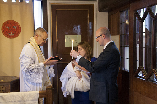 A new dad holds a baptismal candle for his baby, while a priest of the Priestly Fraternity of St Peter celebrates the traditional rites.